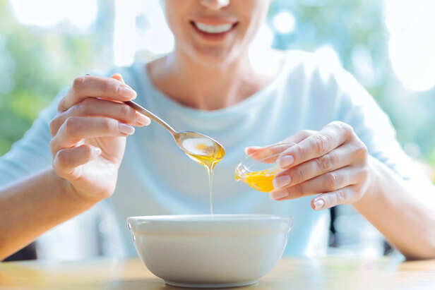 Smiling female adding honey to the porridge